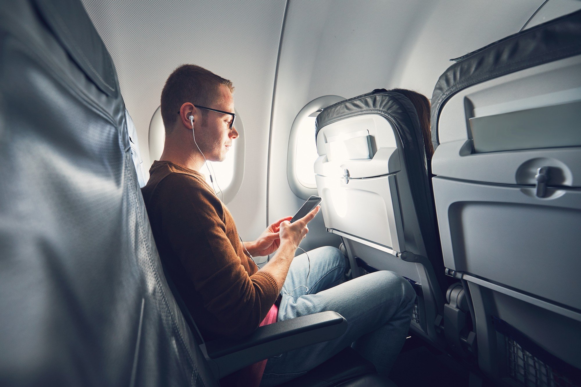 Airplane passenger listens to music on his phone
