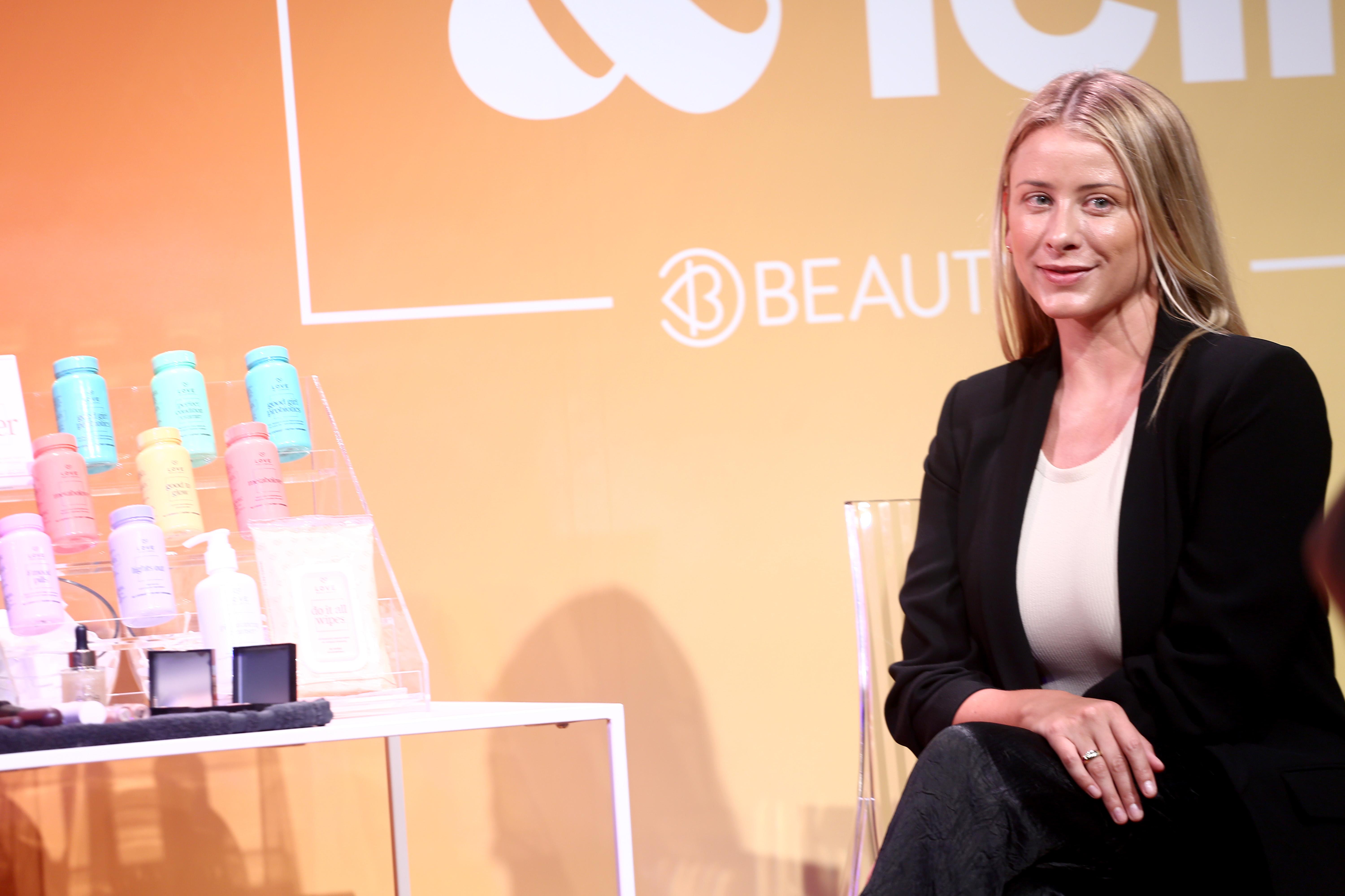 Lo Bosworth sits on a stage at a summit with some of her wellness products