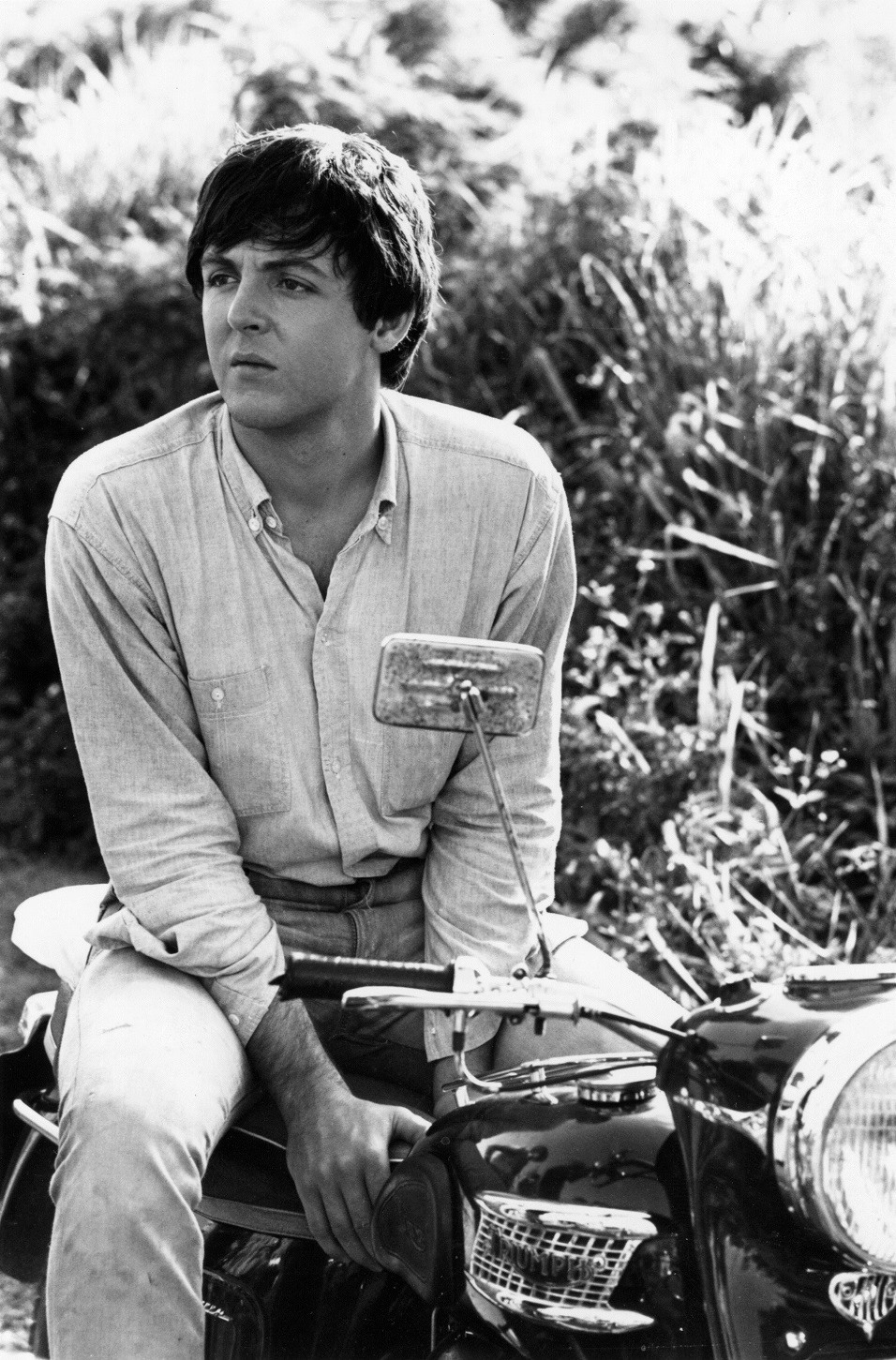 Paul McCartney of The Beatles sitting astride his motor bike, 1965.