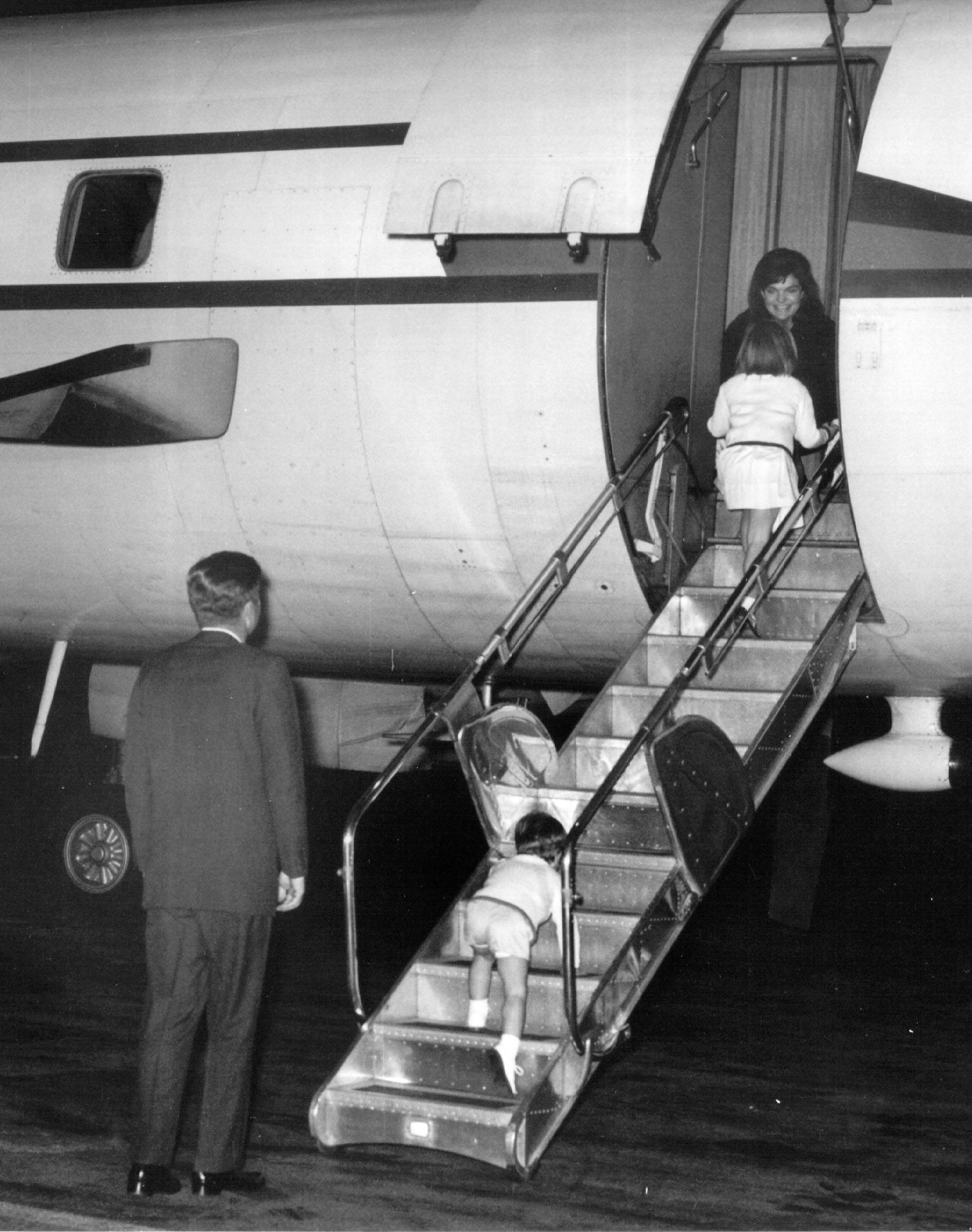 President Kennedy and his children greet First Lady Jackie Kennedy on an airplane