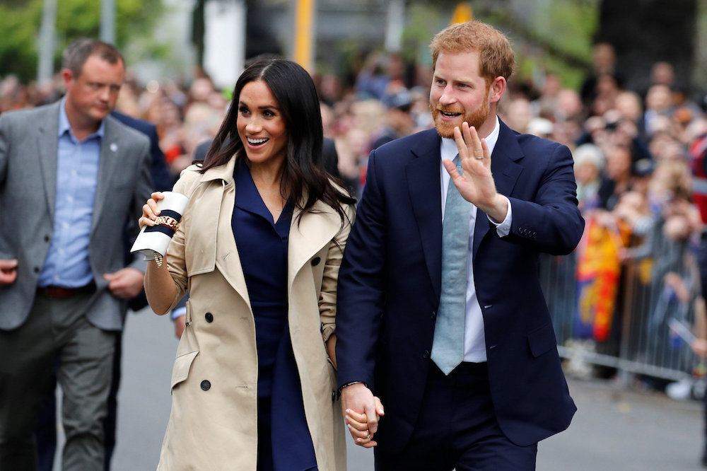 Meghan Markle and Prince Harry waving to a crowd of fans. 