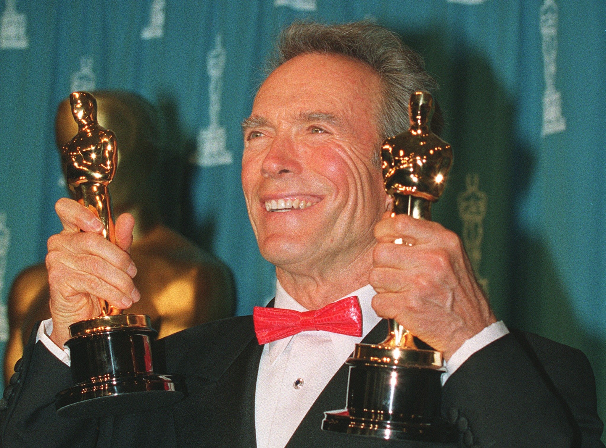 Actor/director Clint Eastwood smiling and holding two Oscars