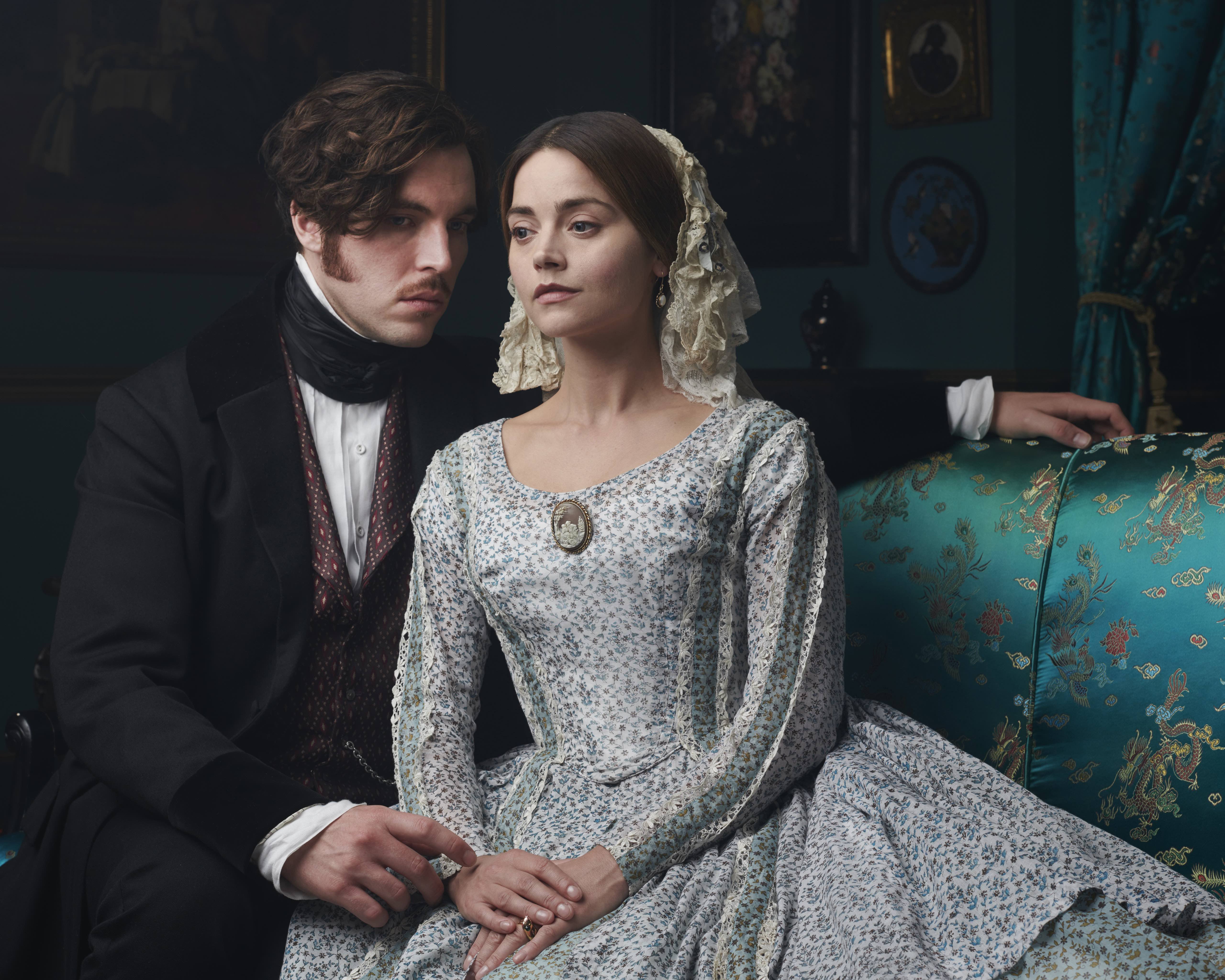 Tom Hughes as Prince Albert and Jenna Coleman as Queen Victoria sitting on a couch 