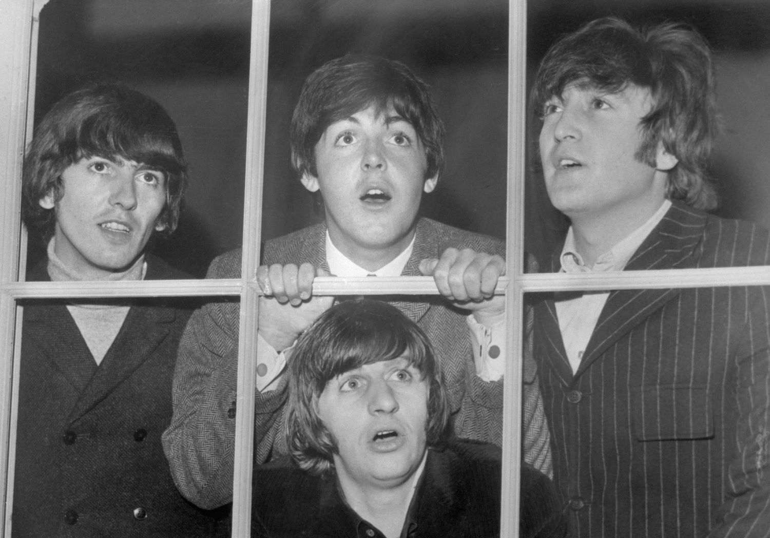 A black and white picture of the Beatles staring through different panes in the same window.
