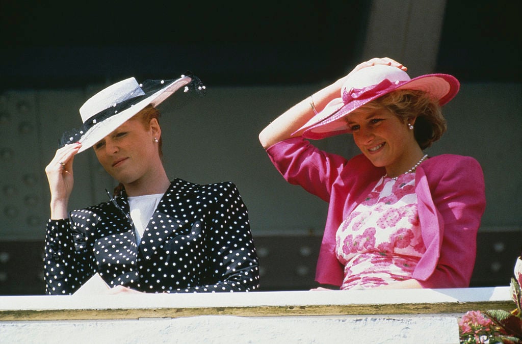 Sarah Ferguson and Princess Diana at a royal event holding their hats down against the wind 