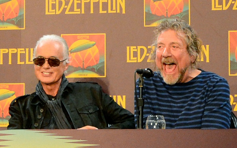 Robert Plant and Jimmy Page sitting behind a microphone at the Led Zeppelin Celebration Day Press Conference in 2012.