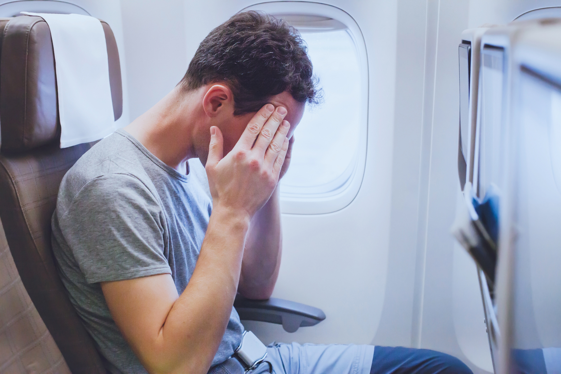 Man on an airplane holding his head