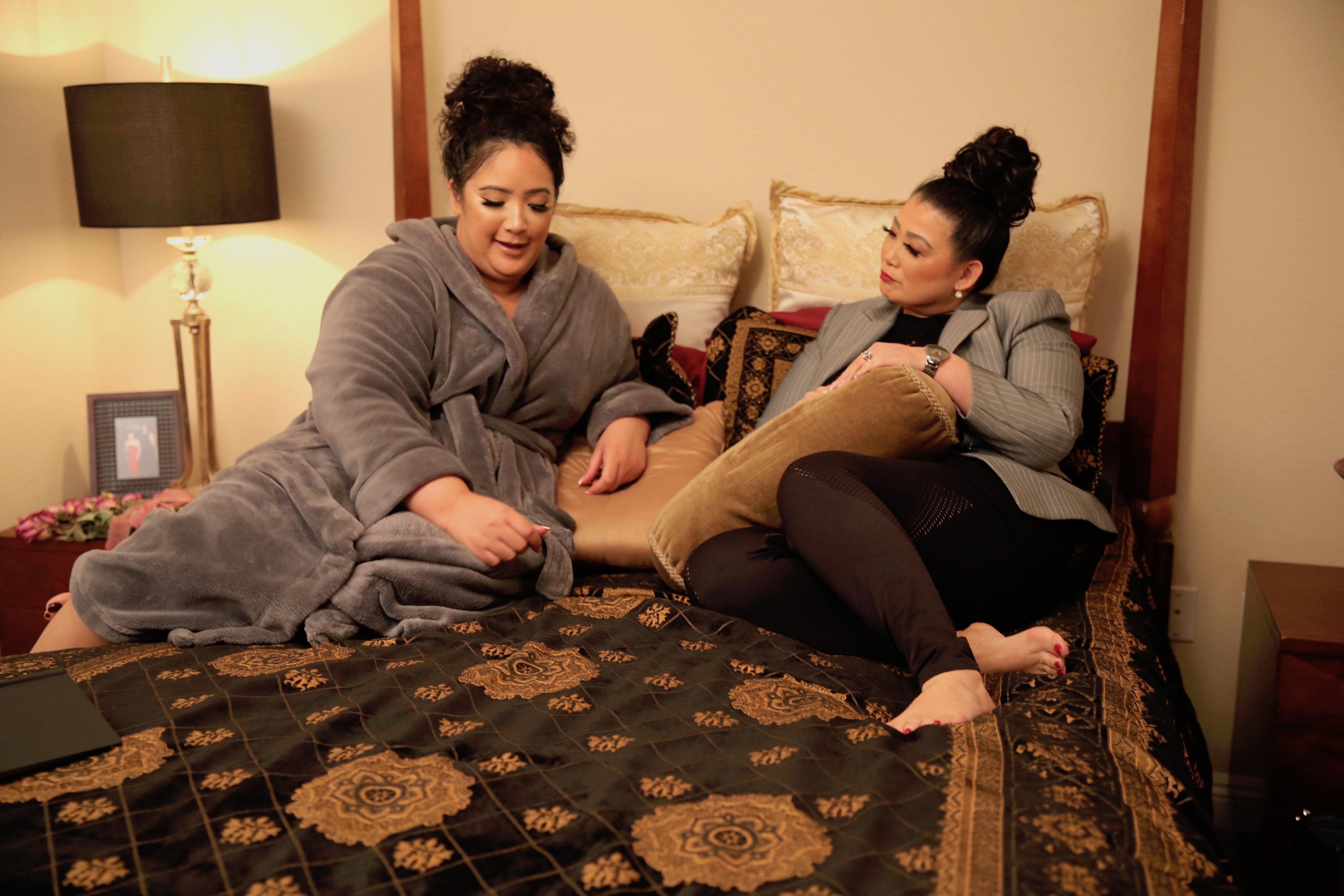 Angelica and Sunhe sitting on a bed in episode of 'sMothered'