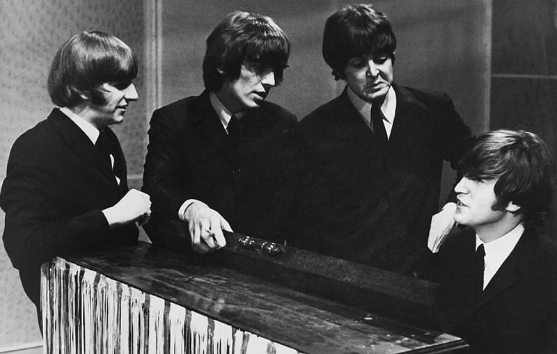 Beatles stand around John Lennon at the piano.