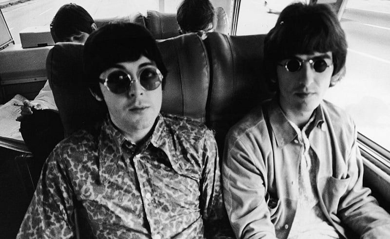 The Beatles' Paul McCartney and George Harrison ride in a bus in 1966.