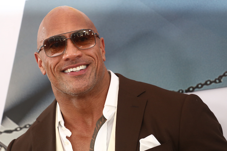 The rock wearing sunglasses smiling at the camera