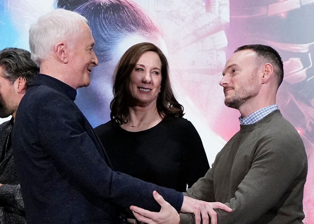 Anthony Daniels (C-3PO) and Chris Terrio share an embrace in front of Kathleen Kennedy at a press conference for 'Star Wars: The Rise of Skywalker.'