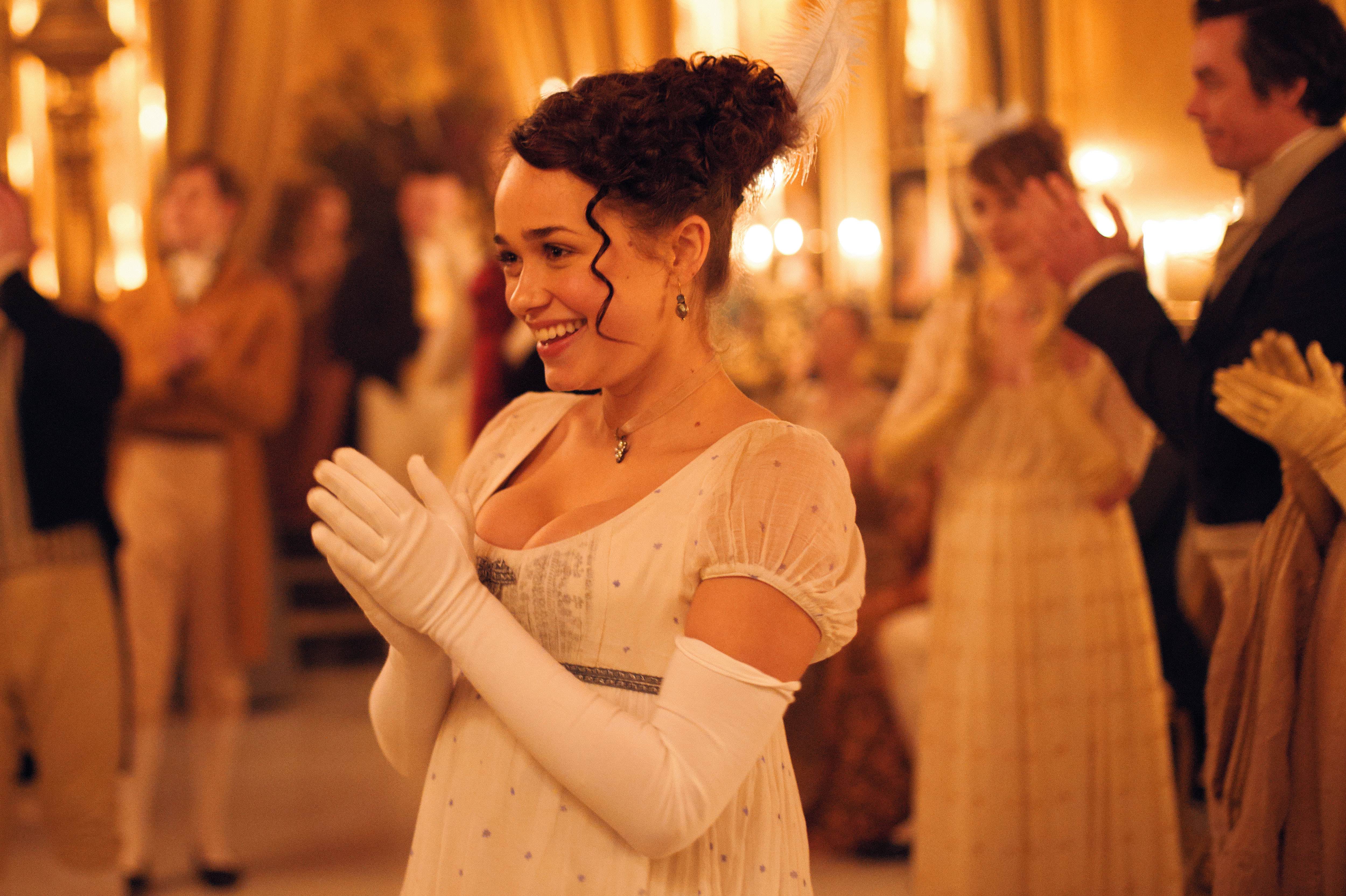 Charlotte, wearing a white dress and gloves and clapping in an episode of Sanditon 