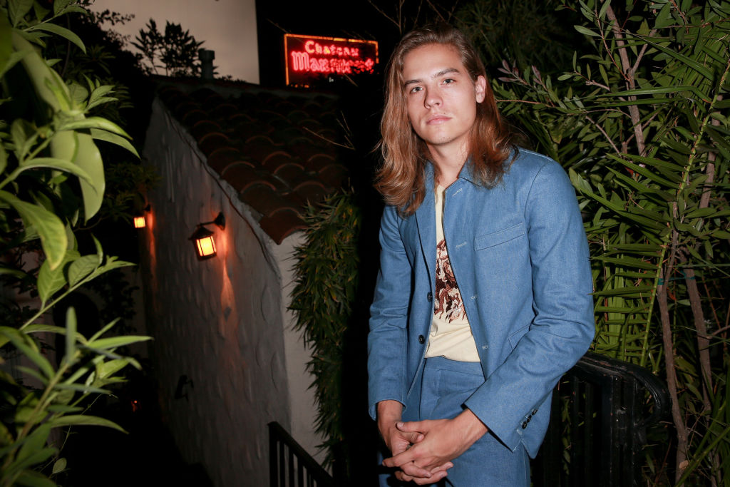 Dylan Sprouse in a blue suit in front of foliage