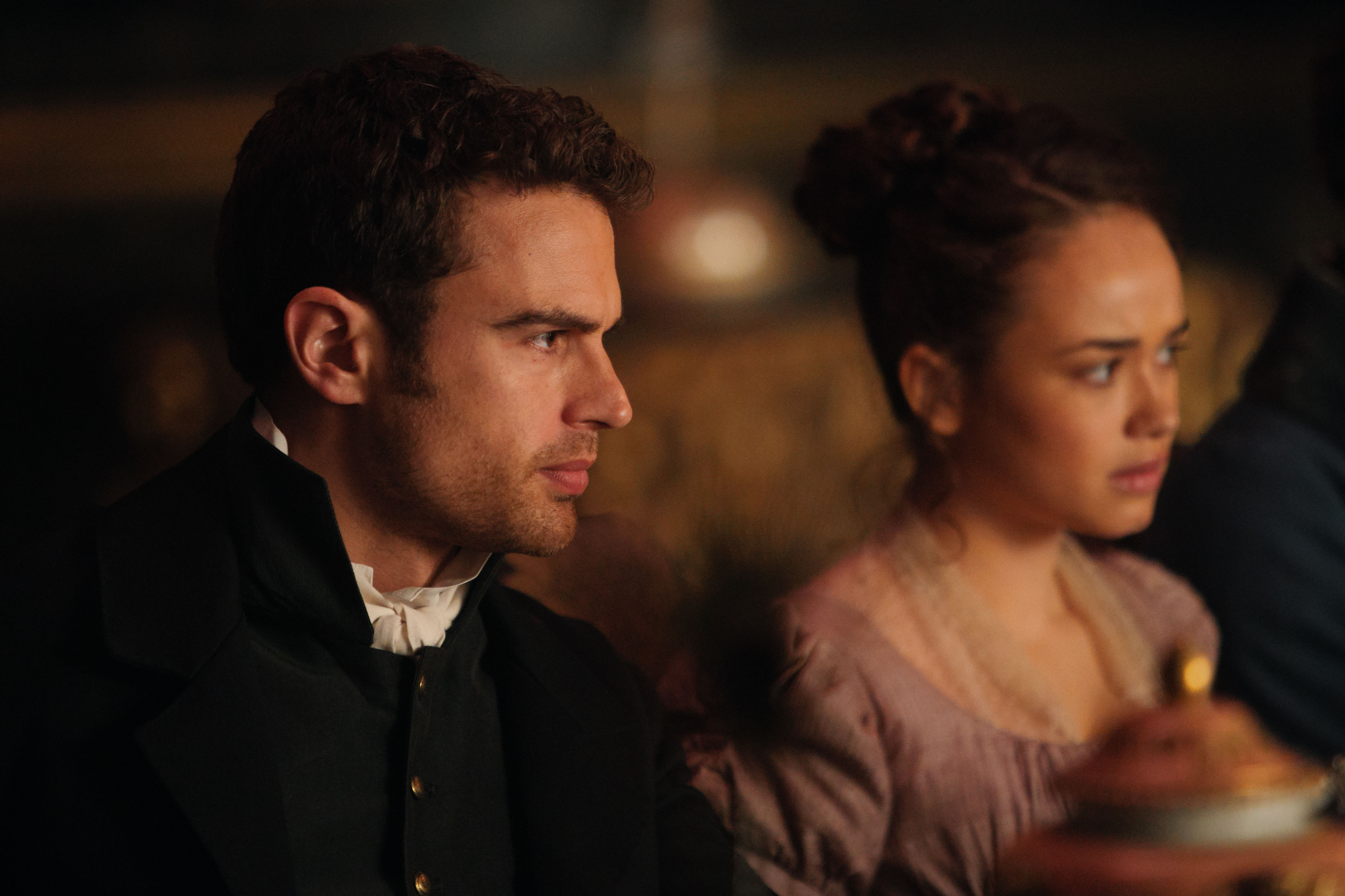 Theo James as Sidney and Rose Williams as Charlotte, in profile and sitting at a table, in 'Sanditon' 