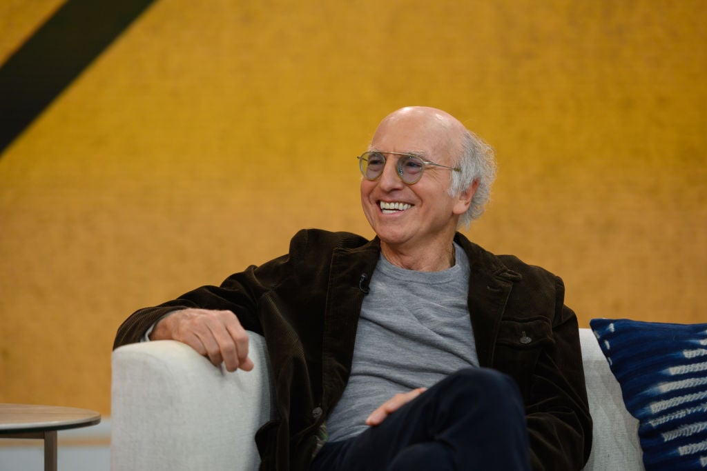 Larry David smiling in an armchair 