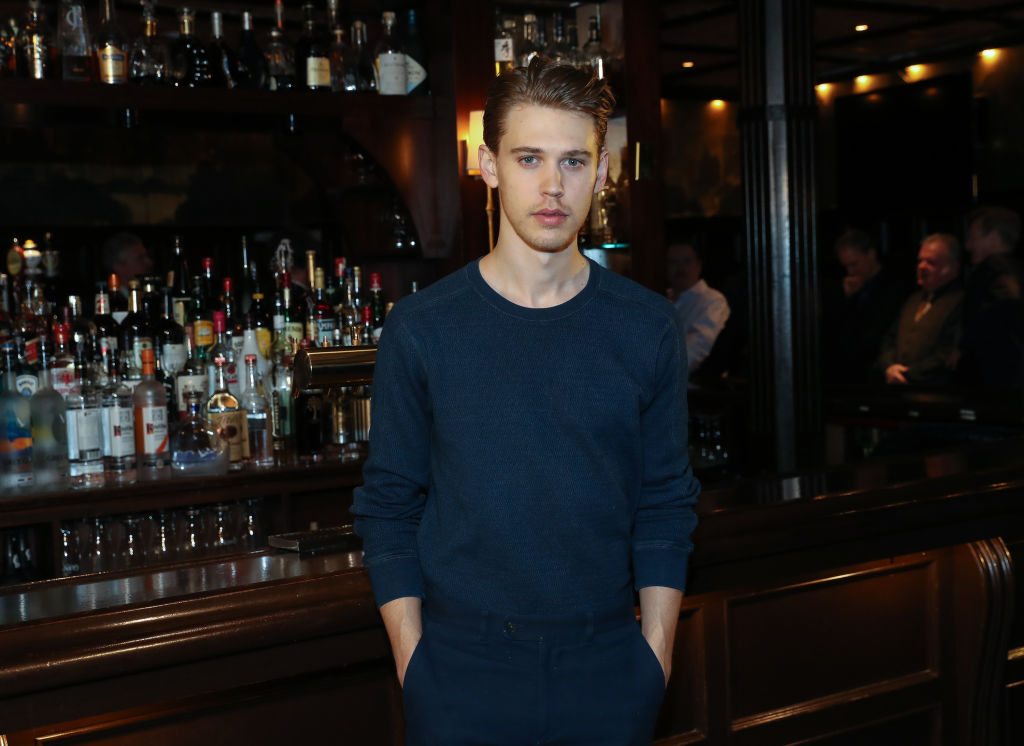 Austin Butler in navy blue standing in front of a bar