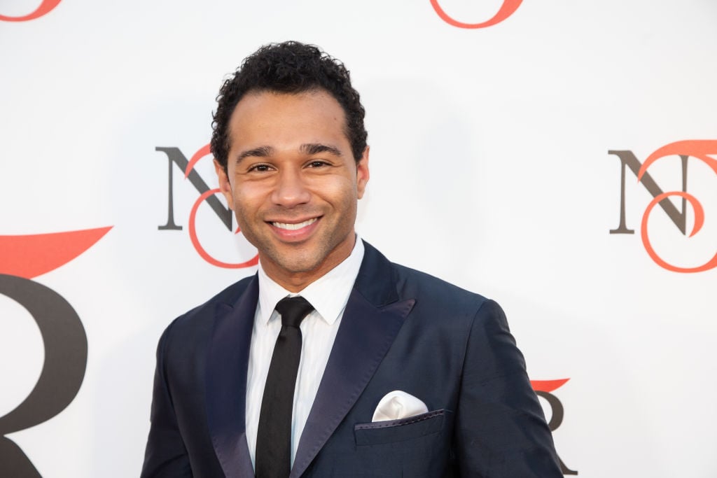 Corbin Bleu smiling in front of a repeating backdrop