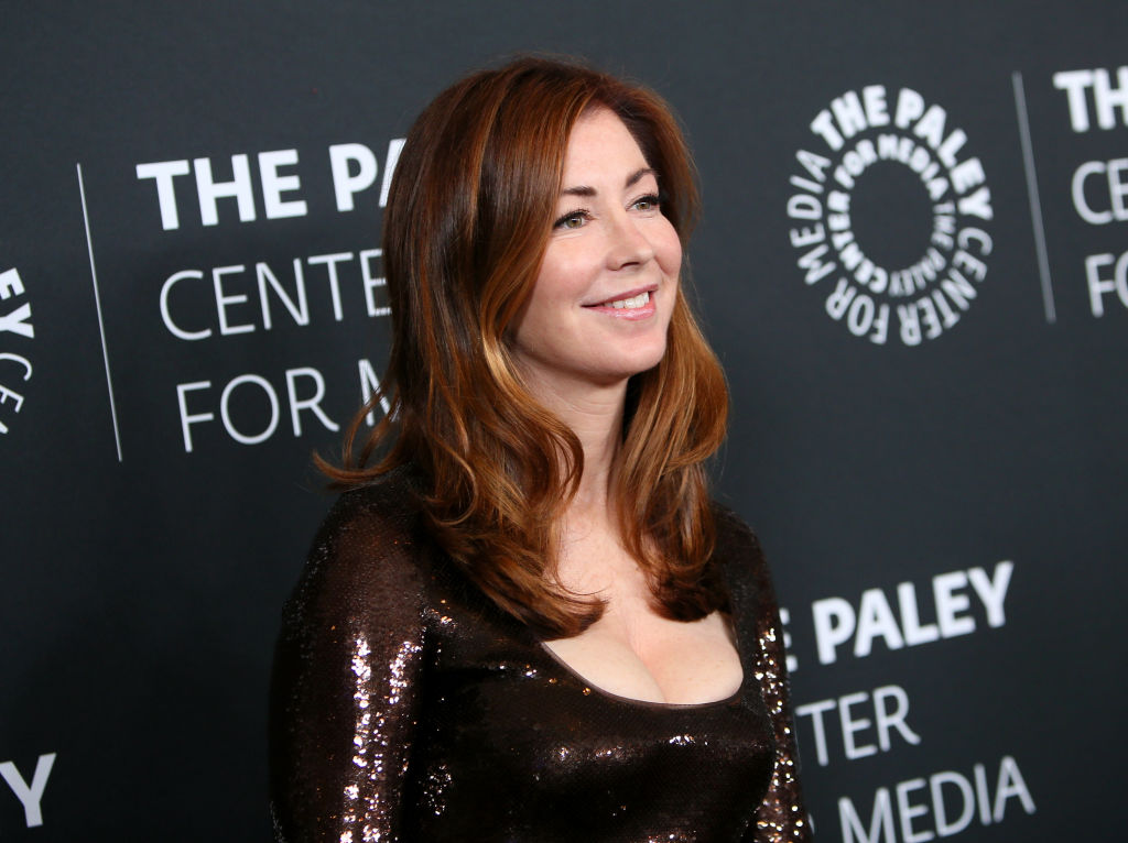 Dana Delany looking off camera, standing in front of a repeating background