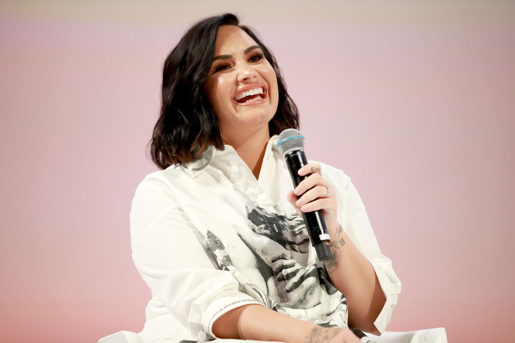 Demi Lovato holding a microphone in front of a pink background