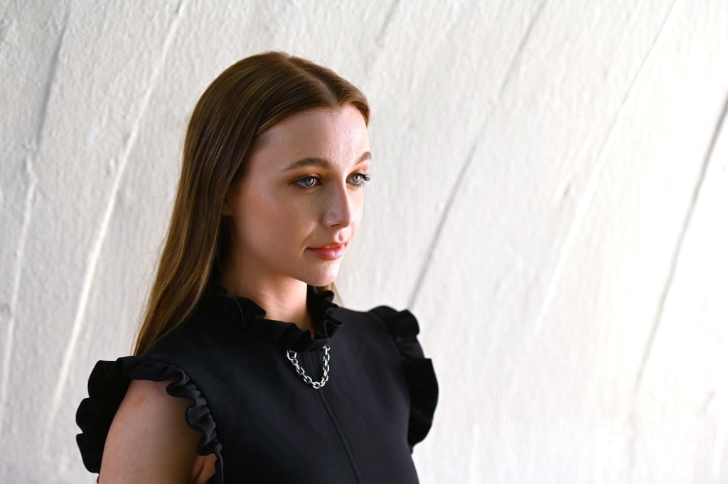 Emma Chamberlin in black in front of a white textured wall looking off camera