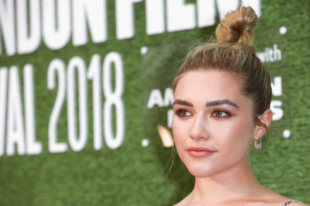 Florence Pugh looking off camera in front of greenery