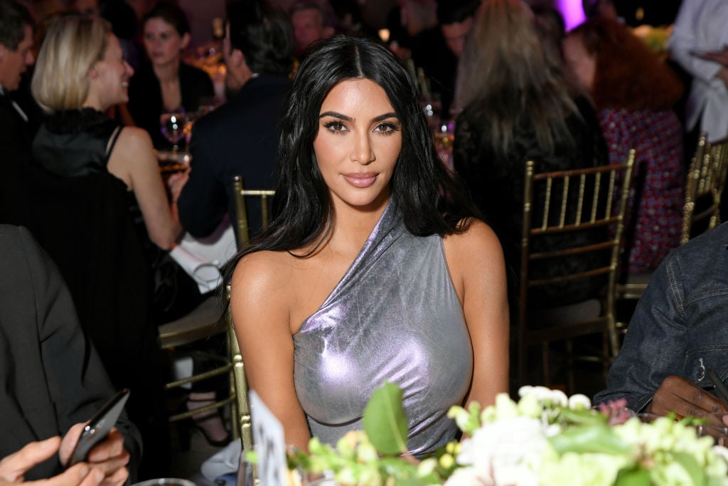 Kim Kardashian in silver, sitting at a table smiling at the camera