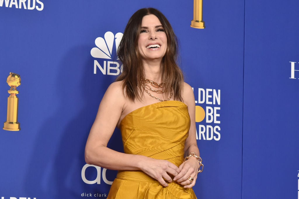 Sandra Bullock in yellow, laughing in front of the Golden Globes repeating background