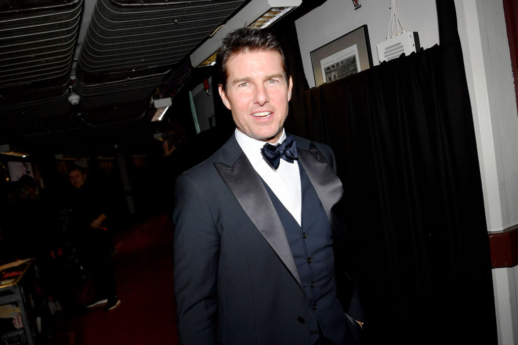 Tom Cruise in a navy suit, smiling at the camera