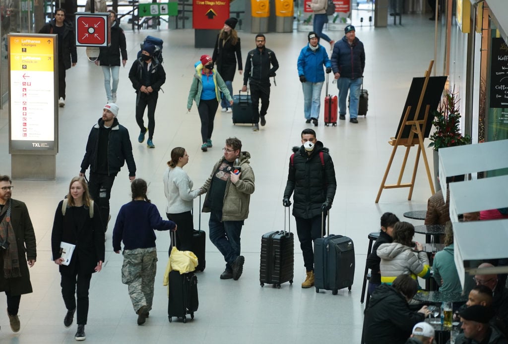Travelers, including one man wearing a protective mask, walk in Terminal A at Tegel Airport before the Trump European travel ban goes into effect