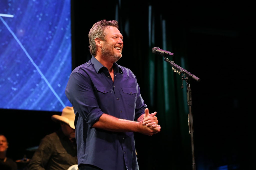 Blake Shelton in front of a microphone, smiling