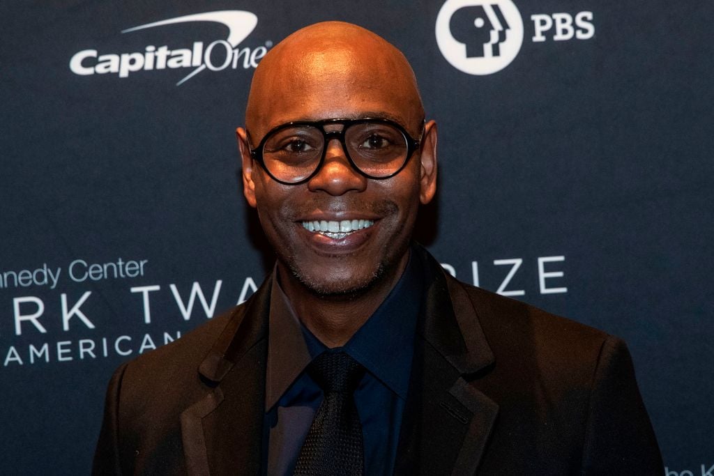 Dave Chapelle smiling in front of a repeating background