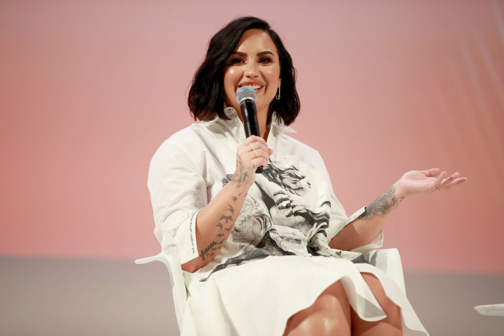 Demi Lovato holding a microphone in front of a light pink background