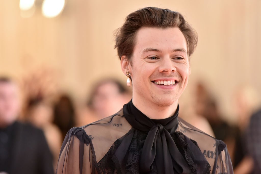 Harry Styles smiling in a high necked sheer blouse with one pearl earring