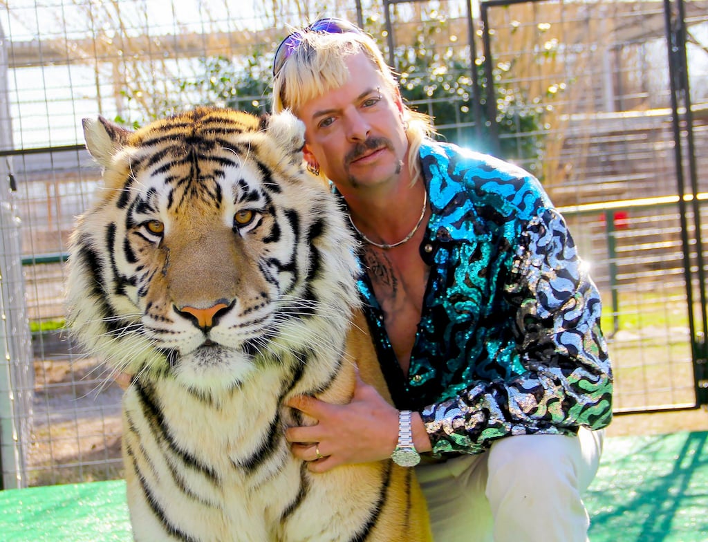 Joe Exotic in a sequined shirt hugging a tiger