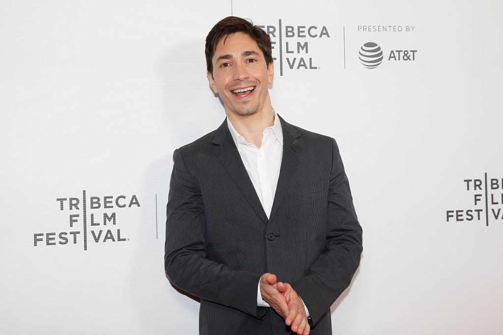 Justin Long smiling in front of a repeating background