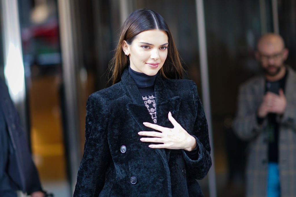 Kendall Jenner in a furry black coat smiling, look down away from the camera