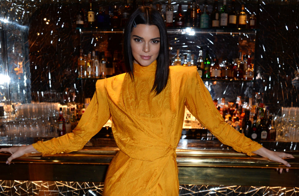 Kendall Jenner smiling with her arms resting outstretched on a bar