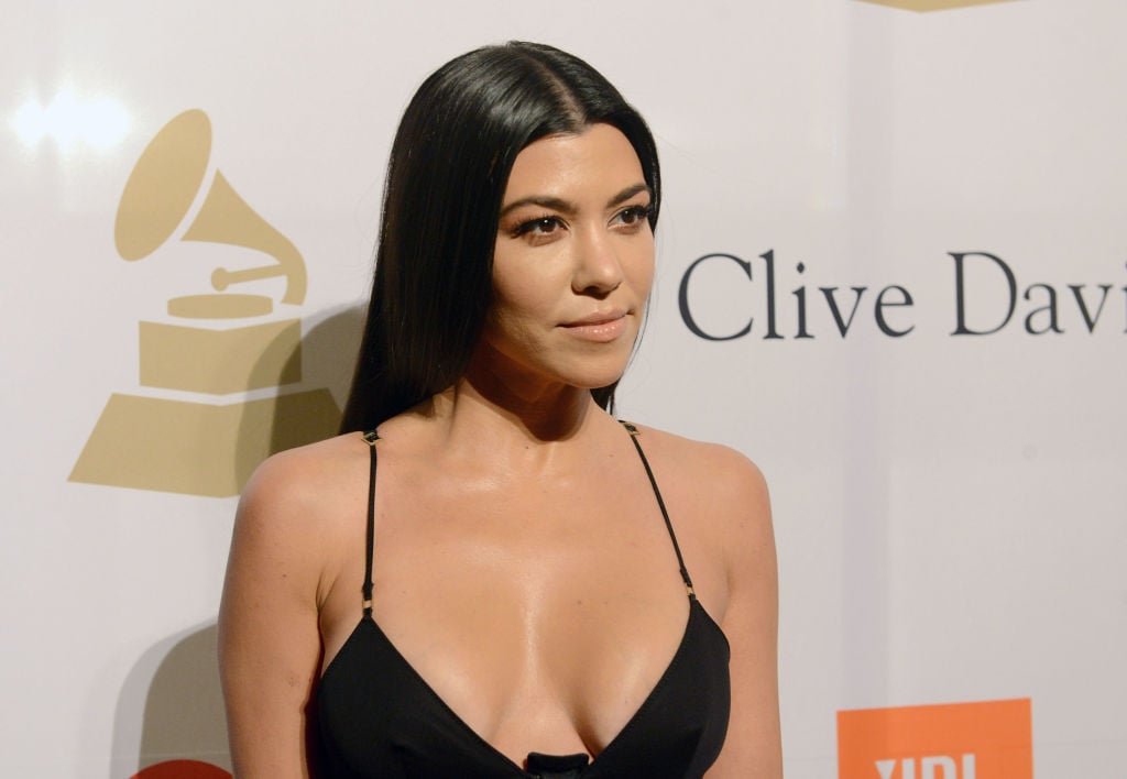 Kourtney Kardashian wearing a thin strapped black dress in front of a repeating backdrop