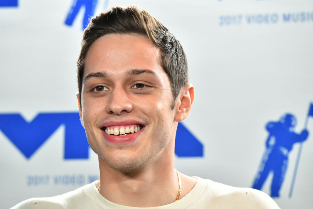 Pete Davidson smiling in front of a repeating background