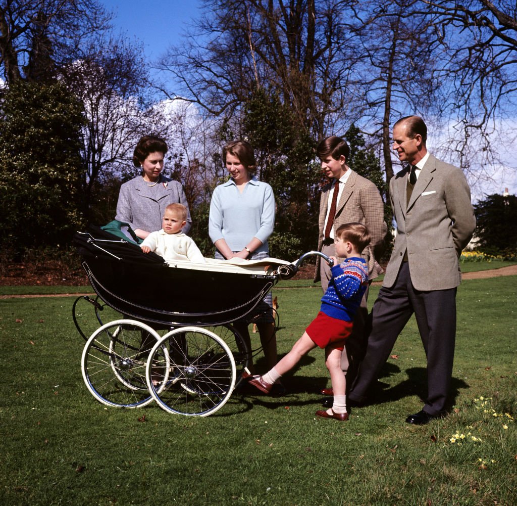 Prince Andrew pushes a baby Prince Edward in a stroller next to Queen Elizabeth II, Princess Anne, Prince Charles, and Prince Philip
