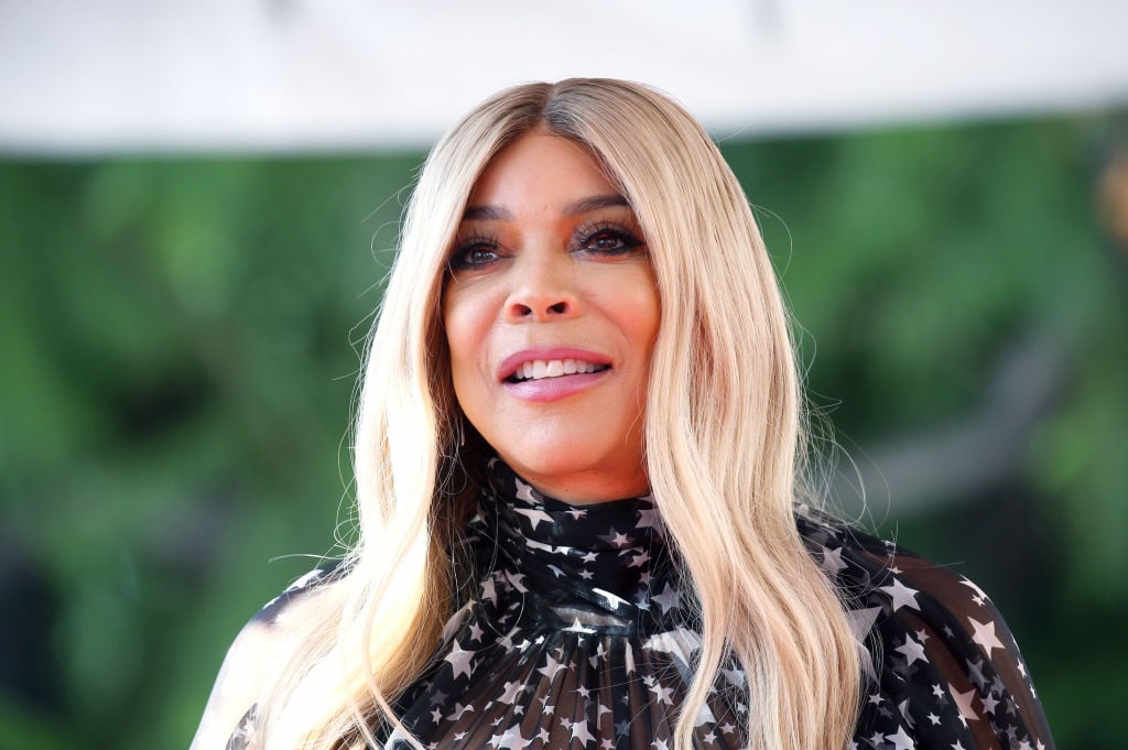 Wendy Williams in a black mock neck shirt standing in front of greenery