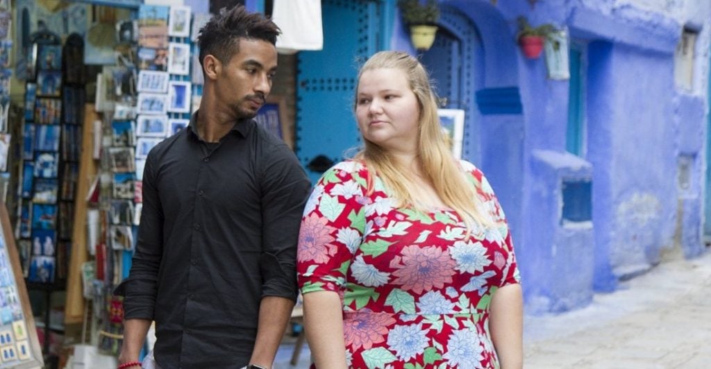 Azan Tefou and Nicole Nafziger of 90 Day Fiancé -- Nicole and Azan pose in front of a blue building, facing away from one another