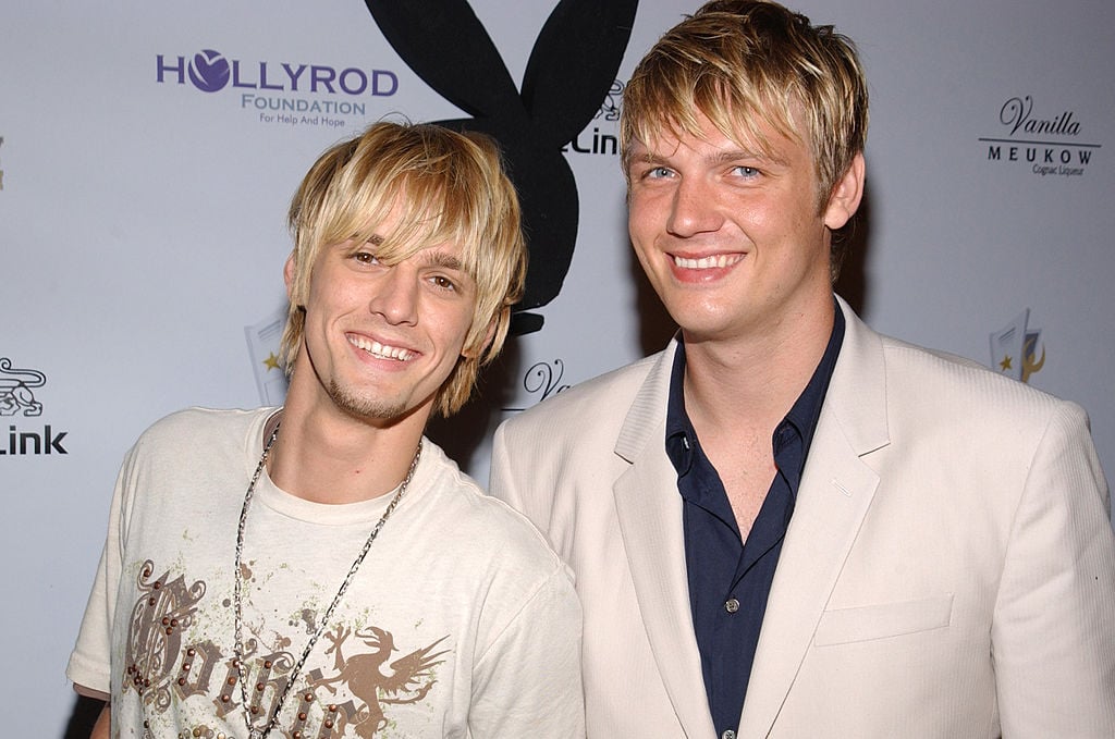 Aaron Carter and Nick Carter smiling in front of a repeating background
