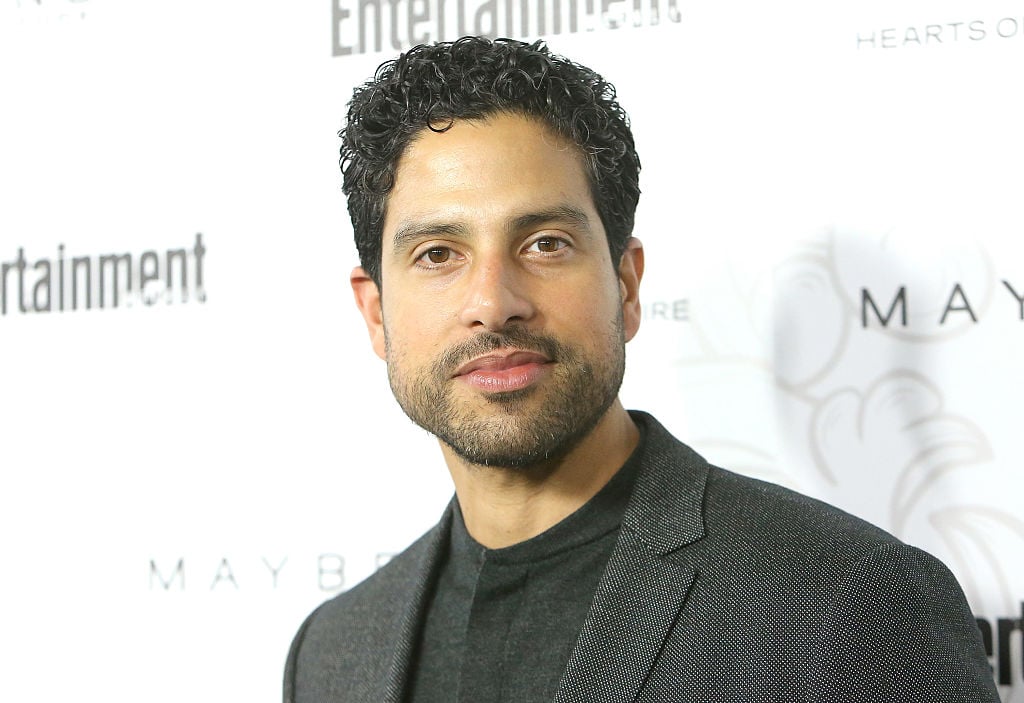 Adam Rodriguez smiling in front of a repeating background