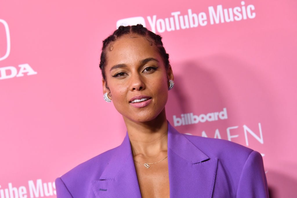 Alicia Keys smiling in front of a repeating pink and white background