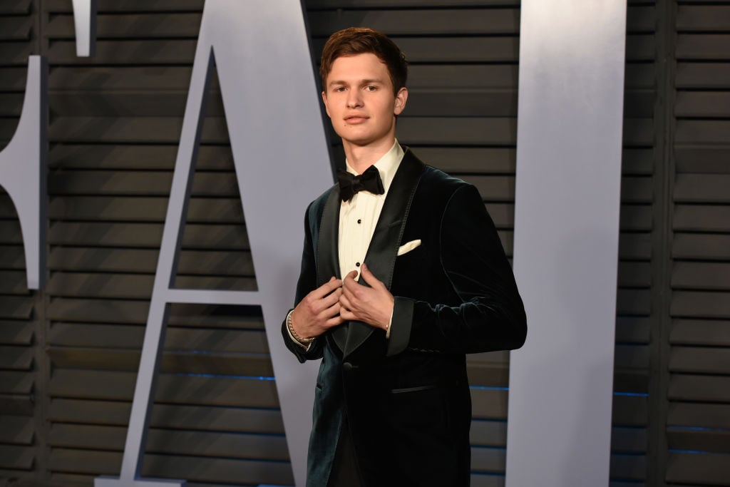 Ansel Elgort in a jacket in front of a repeating background