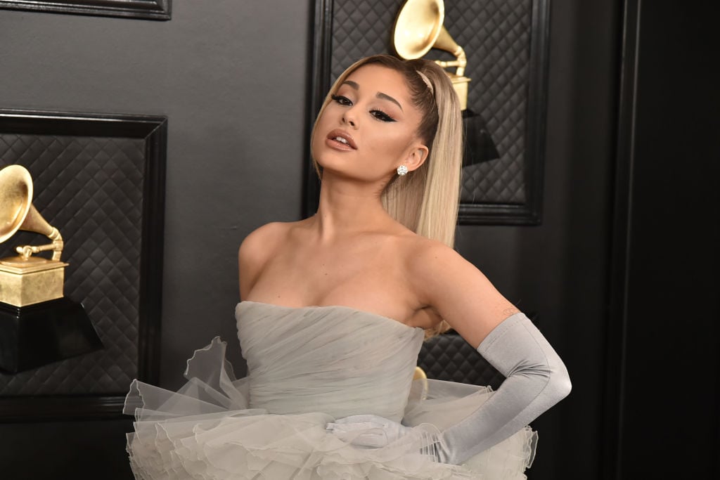 Ariana Grande in front of a repeating background in a gray dress