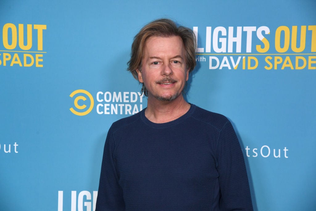 David Spade smiling in front of a repeating background