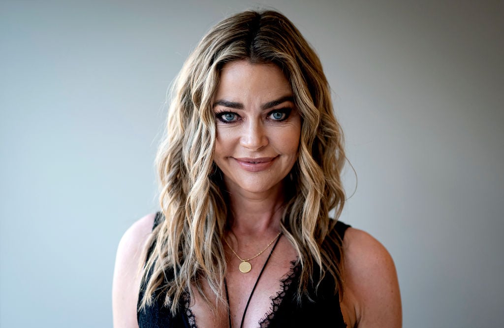 Denise Richards smiling in front of a white backgrounds